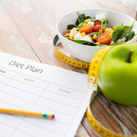 Diet plan sheet next to salad bowl, apple, and measuring tape
