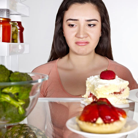 Unhappy woman looking at vegetables on the fridge instead of piece of cake