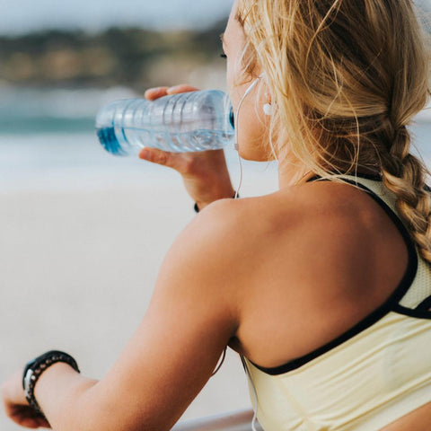 Woman drinking water at the beach after working out