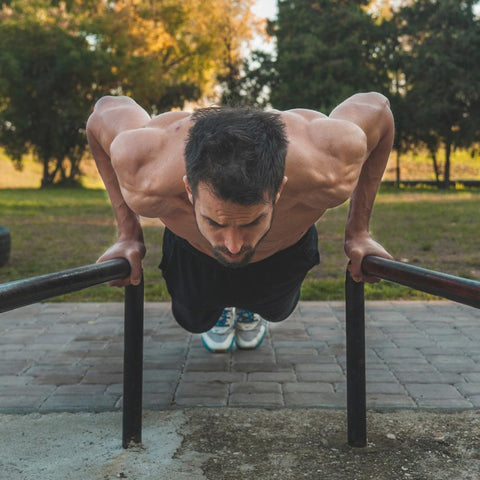 Shirtless muscular man doing calisthenics workout outdoors