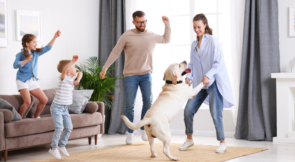 Family with two young kids happily dancing with dog in living room