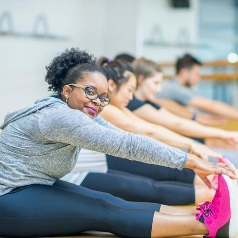 Women smiling at camera while doing stretching exercises in a group class