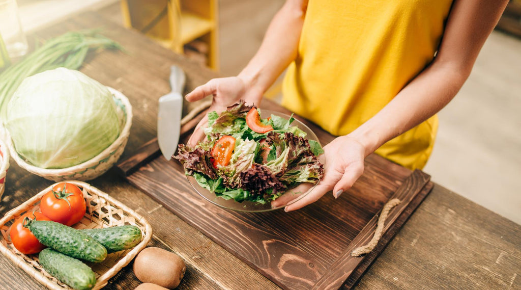 Young woman holding bowl of healthy salad on kitchen counter