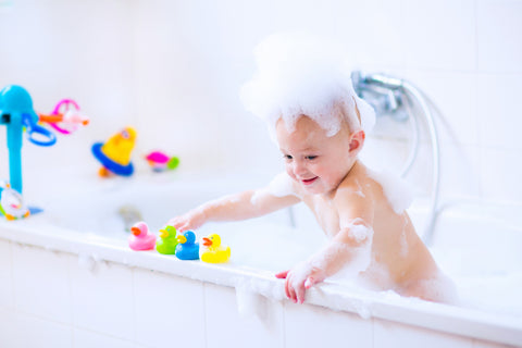 baby covered in bubbles playing with toys during bath time