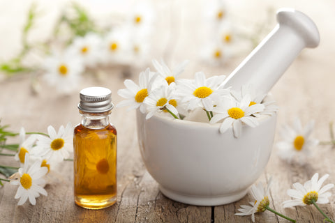chamomile flower in a bowl next to a bottle of oil