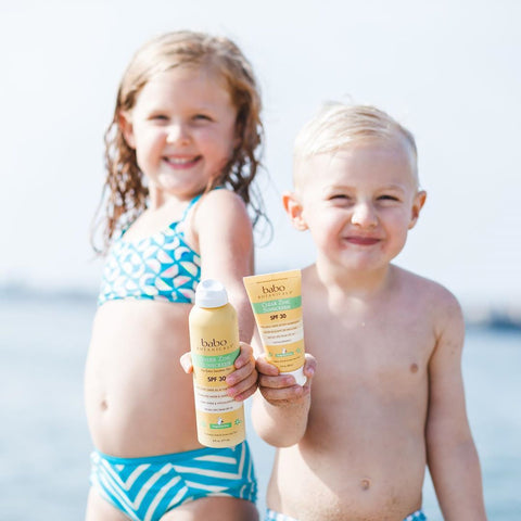 Two kids at the beach holding Babo Botanicals sunscreen with coconut oil