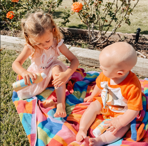 Two kids outside applying Babo Botanticals Sunscreen spray