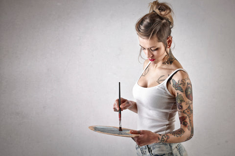 Tattooed woman swirling paint brush on paint palette 