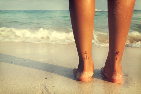 Woman with two small beach themed tattoos on back of ankle