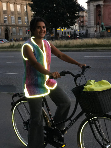 beautiful young woman rides a bike in Copenhagen Denmark wearing a stylish safety vest mohair sweater vest with reflective trim stylish safety at its finest