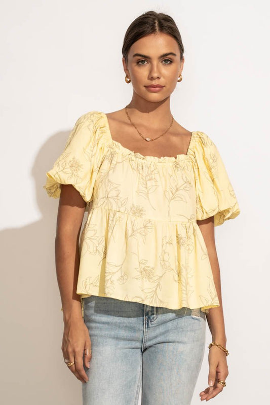 A woman wearing a pair of light was jeans and a yellow floral top,