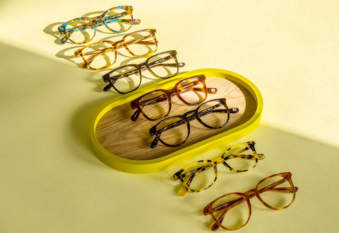 A variety of eyeglass frames laid out on a yellow background