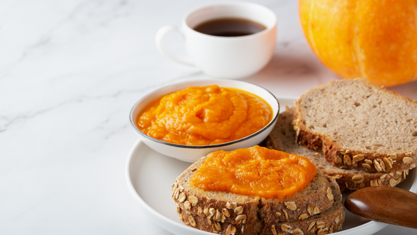 A piece of toast with a bright orange pumpkin spread next to a cup of coffee