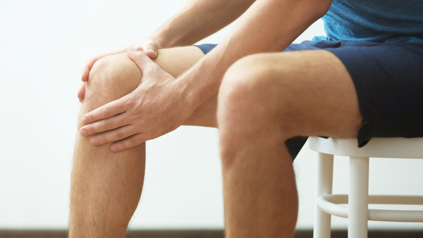 Probiotics can help with inflammation. Photo of a seated man's legs - he is wearing shorts and holding one knee as if it hurts.