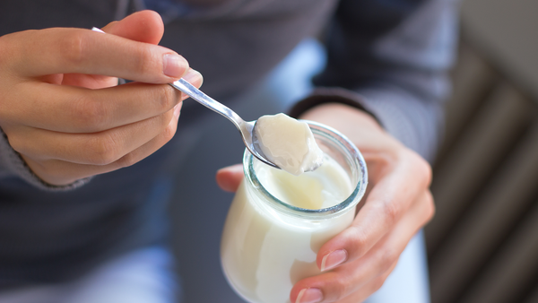 A person is spooning plain yogurt from a glass jar