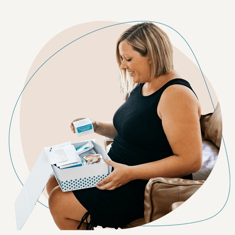 A pregnant lady holding a baby shower gift by belly bands.