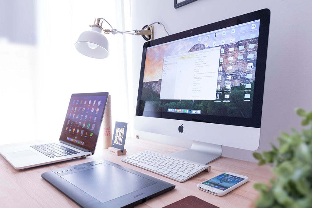 imac, laptop, iphone, and wacom tablet on a wooden desk with a white wall behind