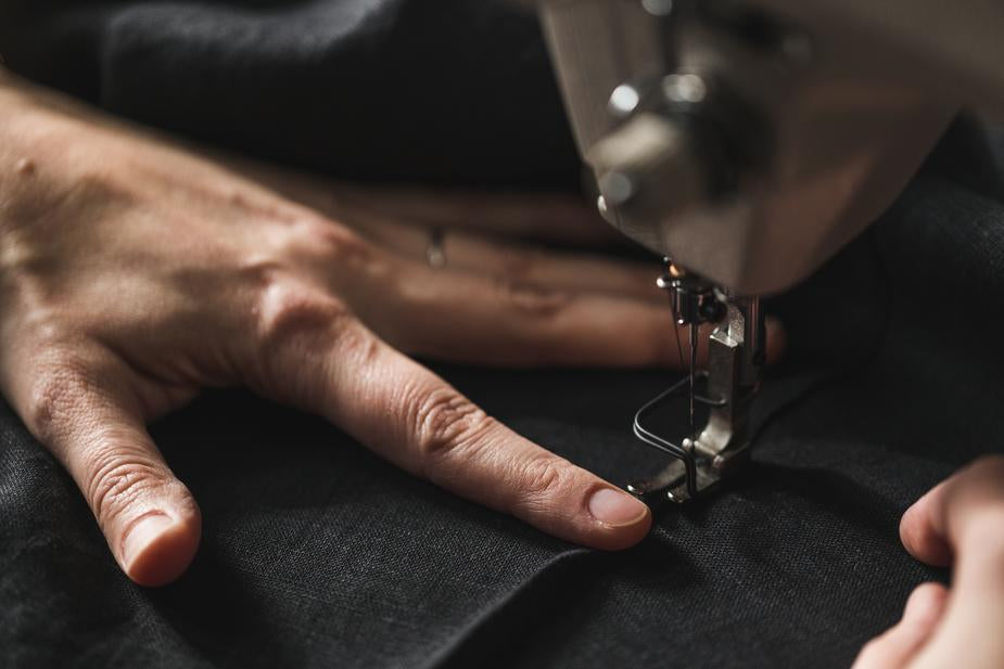 image of woman's hand close up feeding black fabric through a sewing machine