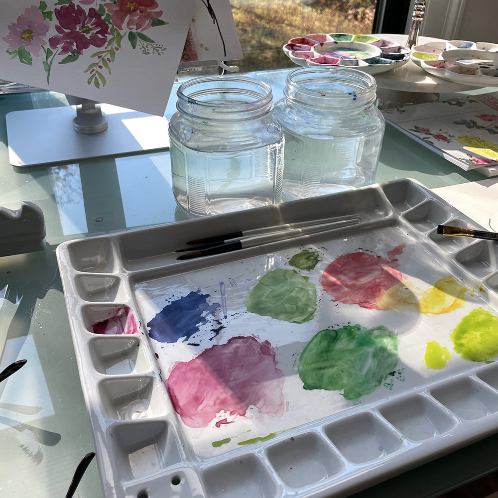 studio table with watercolor palette, paints, and light streaming in