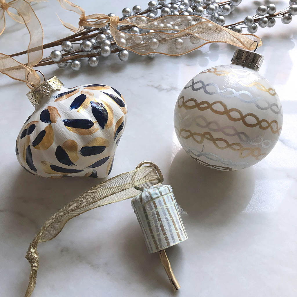 hand-painted glass Christmas ornaments on a white surface. Designs are abstract and are blue, white and gold