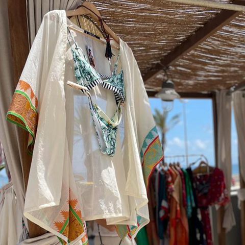 A white jacket on a hanger with a floral and striped bikini underneath