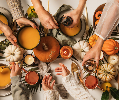 People sharing soups at a table with pumpkins for a fall dinner party.
