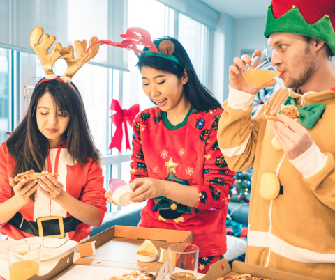 Friends dressed up in Christmas themed costumes while eating pizzas and drinking beverages at a holiday party.