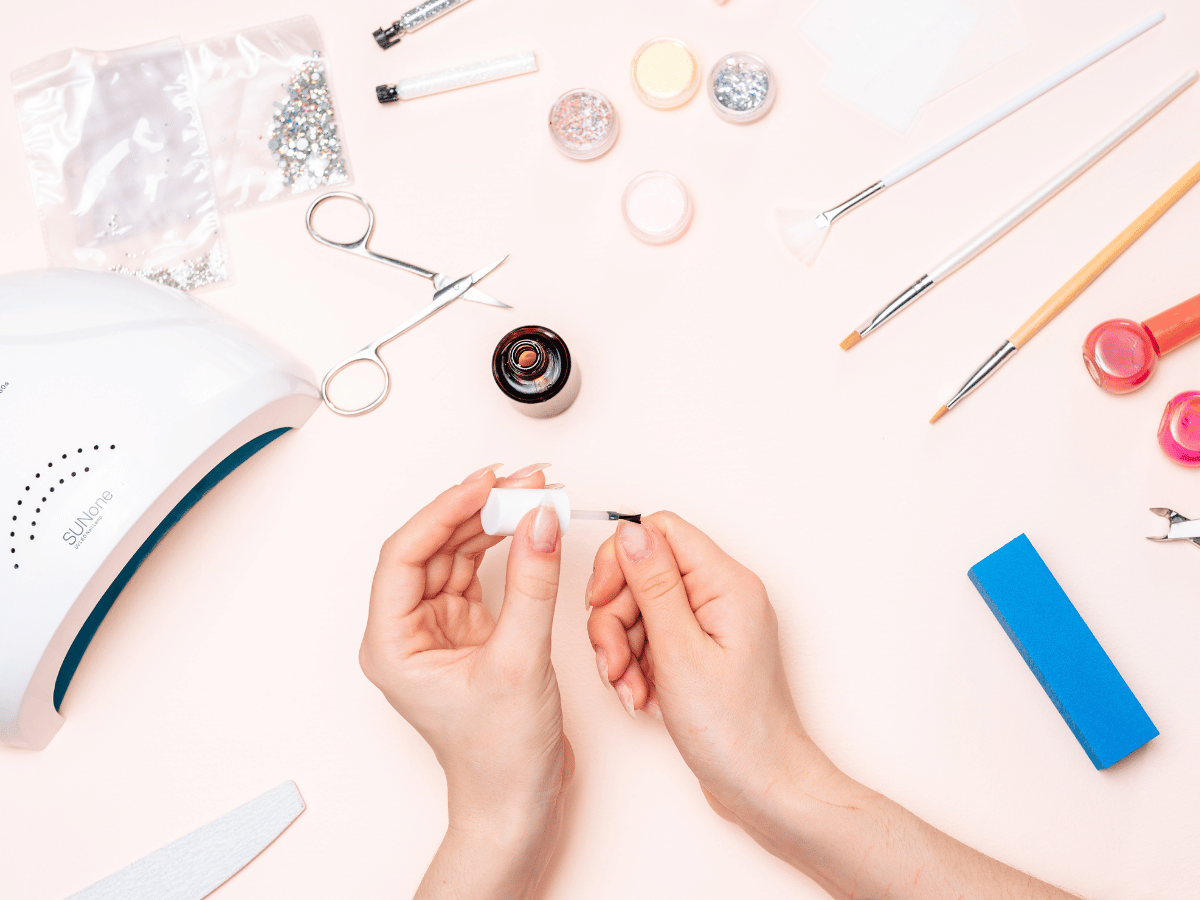 Top down view of a person doing their own nails with nail tools and accessories on the surface.