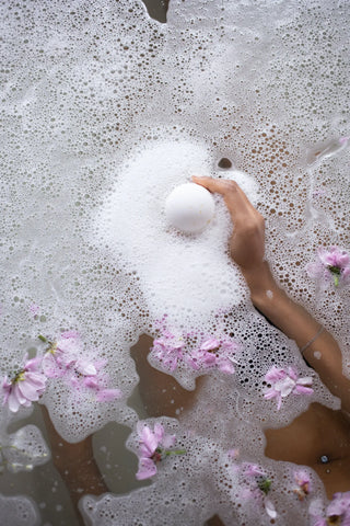 bath bomb fizzing in a bath with flowers floating in the water