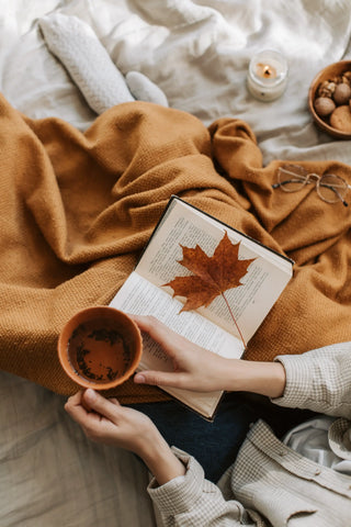 sipping tea and reading a book with fall maple leaf as a bookmark