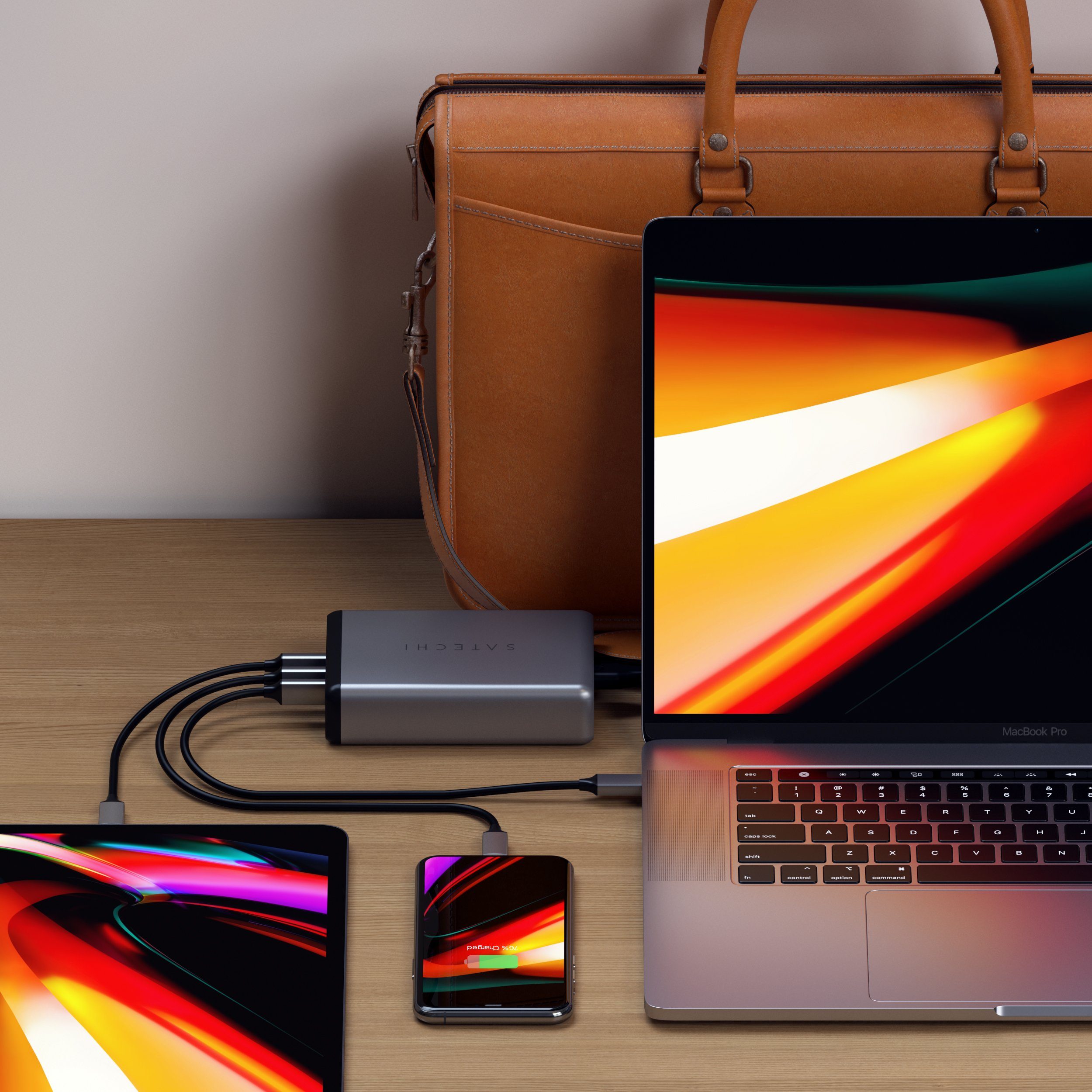 Satechi 108w pro usb-c pd desktop wall charger on a desk simultaneously charging a MacBook Pro, an iPhone, and a iPad Pro in front of a work bag