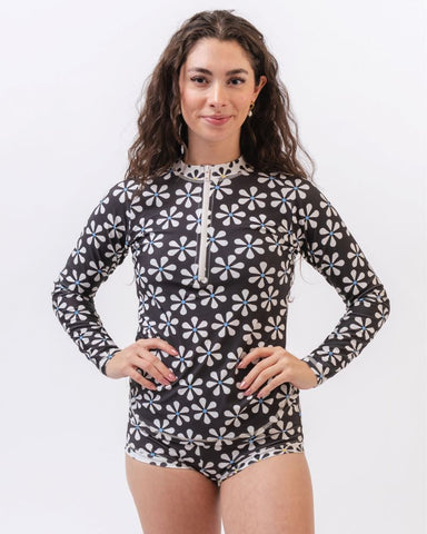 Photo of a woman wearing a black and white floral rash guard swim top and a black and white floral swim bottom