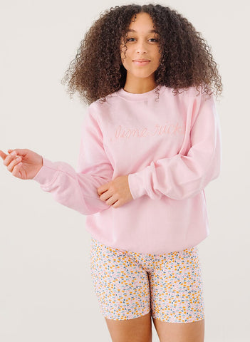 woman in a pink oversized crew neck sweatshirt with Lime Ricki embroidered in cursive on the chest