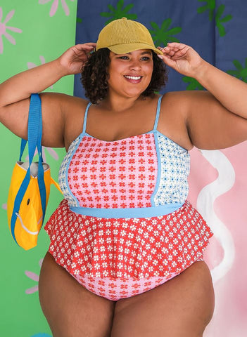 woman in plus size peplum swim top and matching high waist swim bottoms, smiling and adjusting a hat