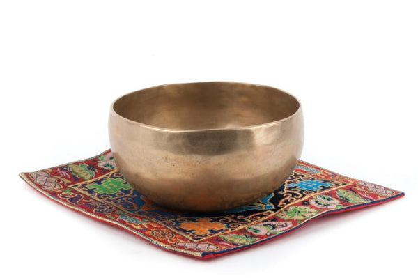 plain singing bowl placed on a red mat with colorful embroidery