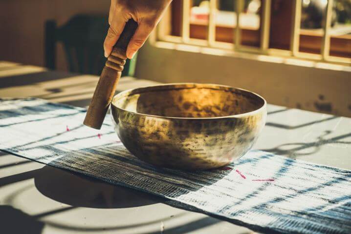 hand holding wooden mallet circling rim of a medium sized singing bowl