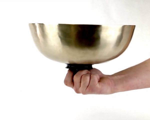 large plain gold singing bowl hand grasping black handle on the bottom