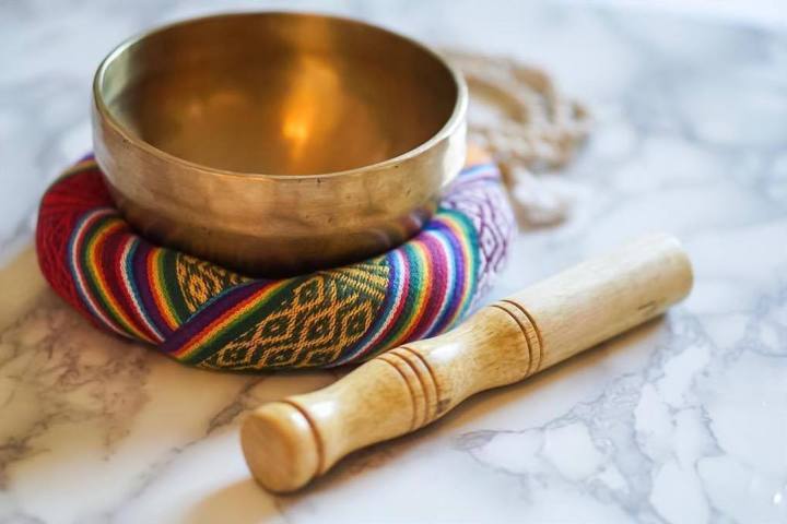 singing bowl on top of a colorful pillow wooden mallet placed on a white marble surface