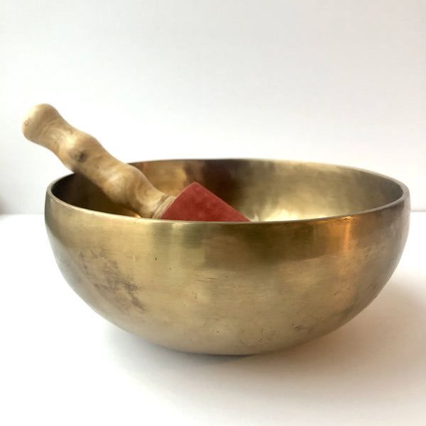 large plain gold singing bowl with wooden mallet covered with suede red fabric