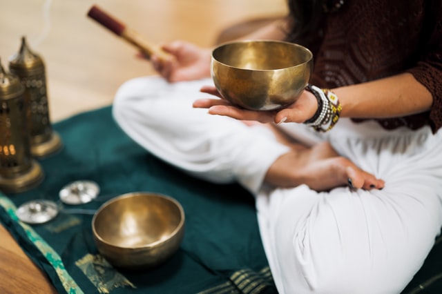 person sitting in a lotus position holding mallet in one hand and singing bowl in the other