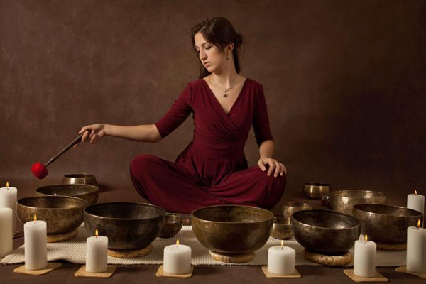 woman wearing red dress surrounded by singing bowls and white candles