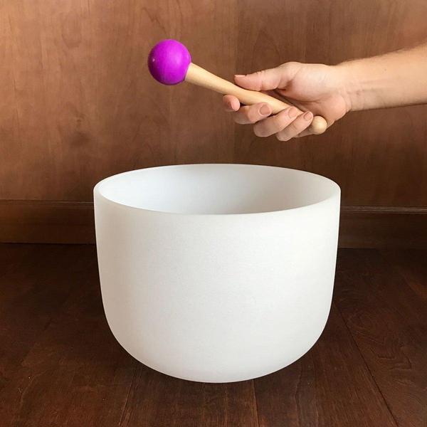 hand holding wooden mallet with purple ball jointed tip white crystal singing bowl underneath