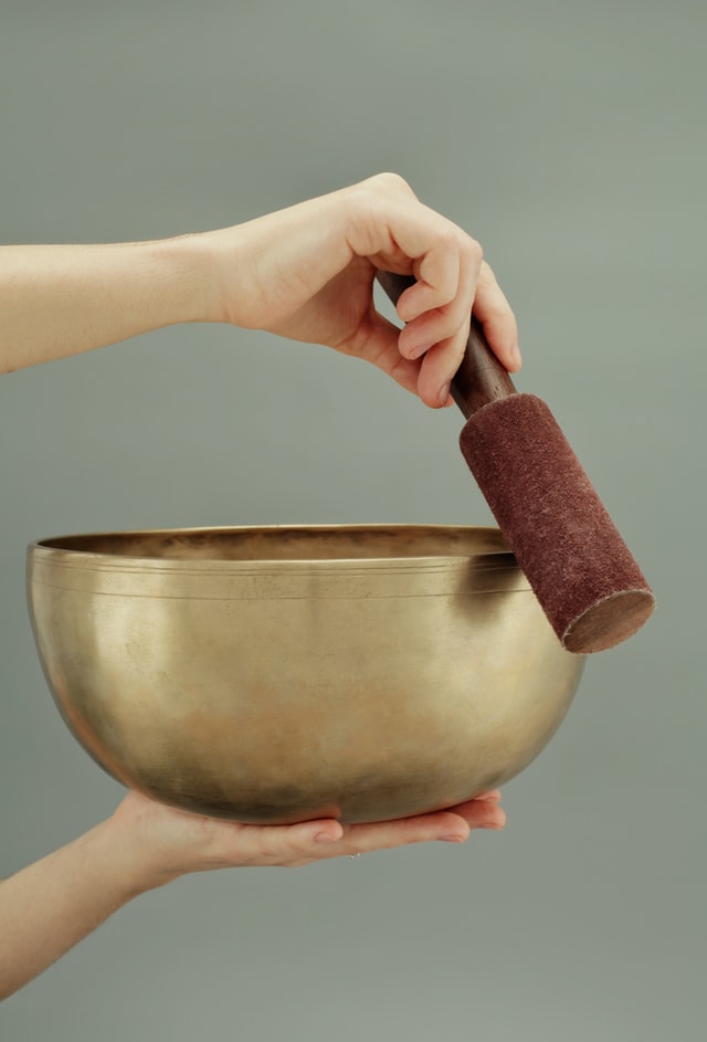 one hand holding singing bowl other hand holding mallet circling the rim