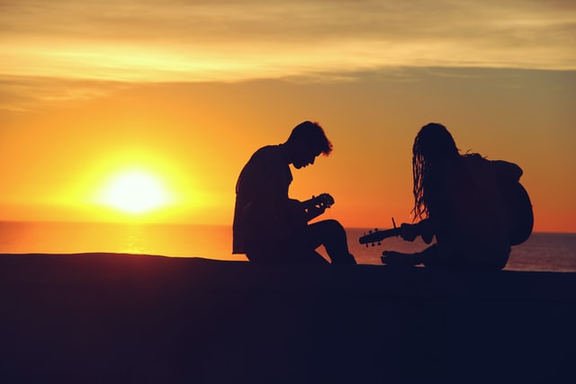 silhouette of two persons playing musical instrument sunset behind them
