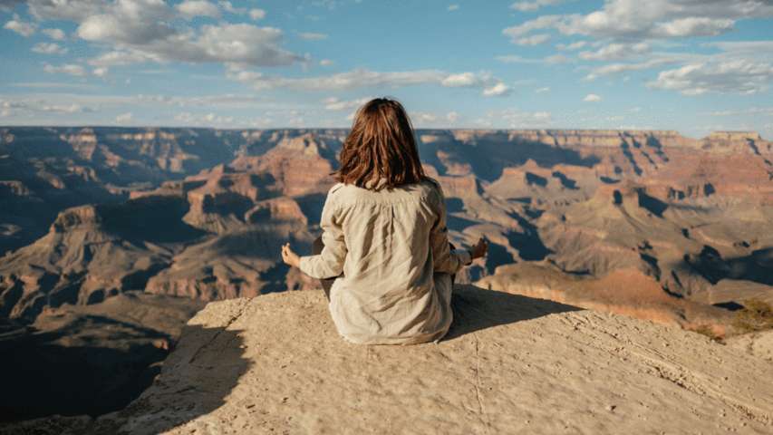 woman sitting in lotus position facing canyon