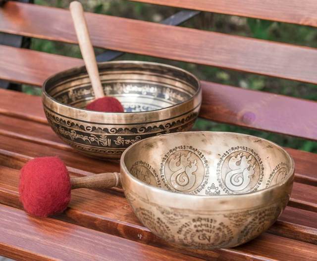 two gold singing bowls with elaborate design and writings inscription two mallets with red suede cover