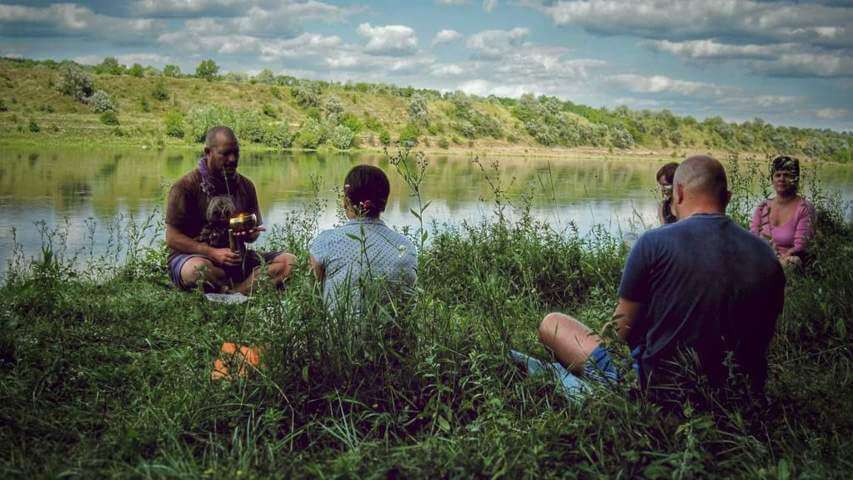 group of people sitting on a field of grass near riverbed