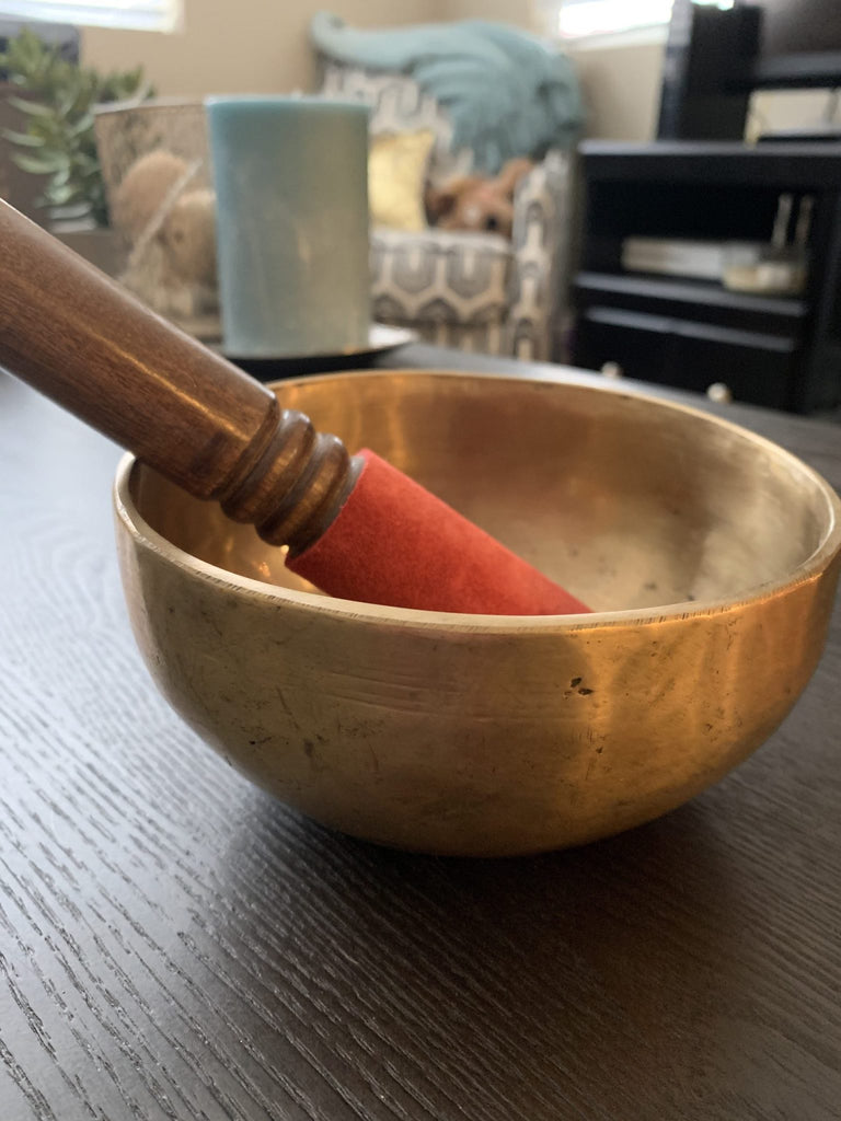 medium sized plain singing bowl Shanti Bowl wooden mallet red suede cover placed on a wooden surface