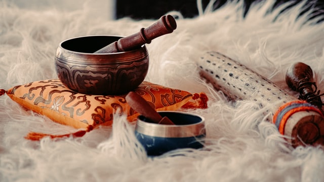 two singing bowls with etched design placed on a yellow pillow and fluffy white rug
