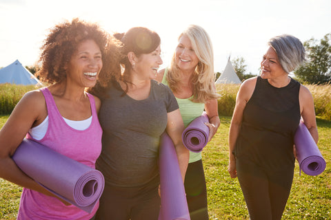 Four women laughing and walking to yoga class with their pats in hand